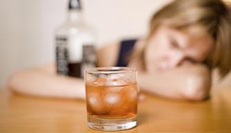 Alcoholic woman with a bottle of liquor staring at a glass of whisky