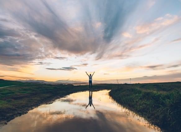 Man standing at river in the sunset with arms outstretched