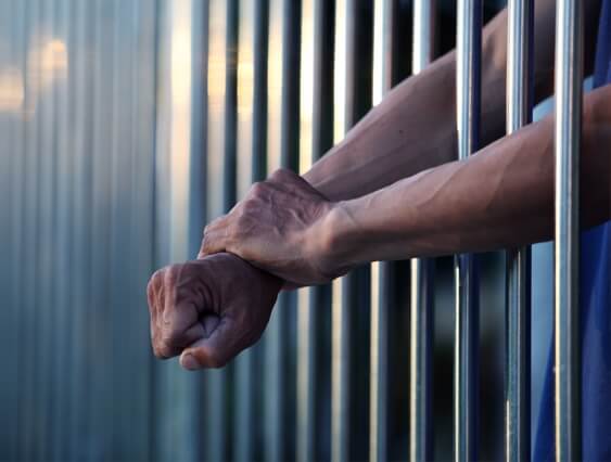 Man with his arms through his jail cell.