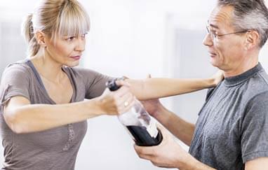 Wife taking a liquor bottle away from her alcoholic husband