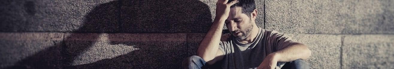 Man sitting in a dark alley with his head in his hand