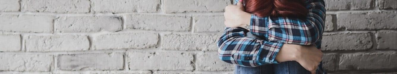 Girl with her head down hugging her knees in an alley
