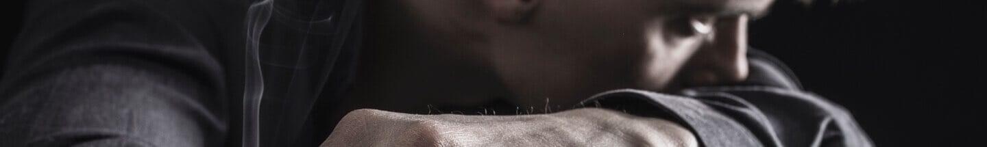 Man smoking a cigarette resting face on his arm