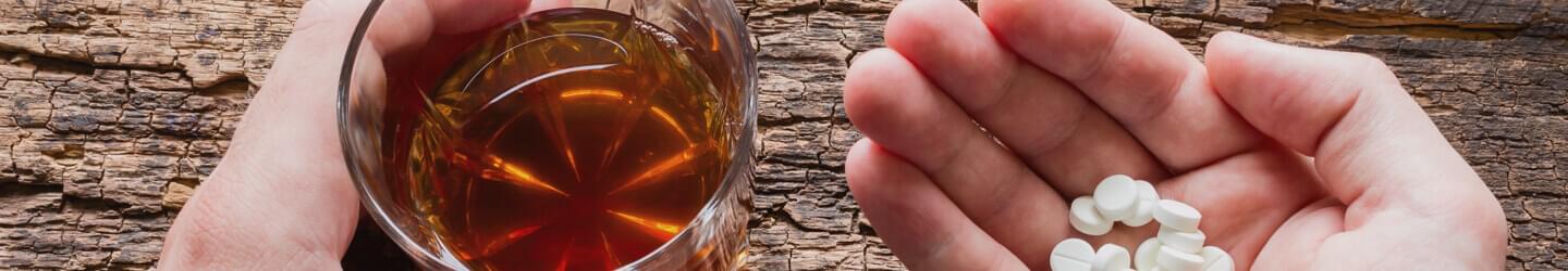 A persons hand with pills in them next to a glass of liquor