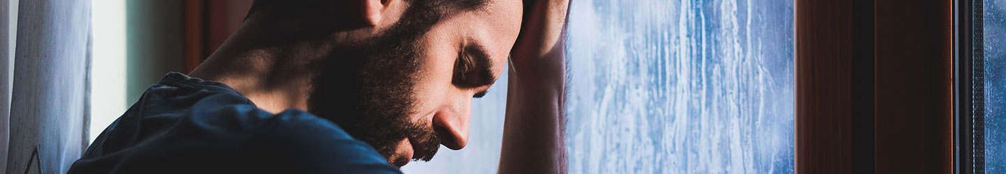 depressed man infront of a window palming
his forehead