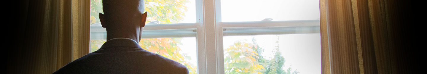 man in suit staring out a window in his home