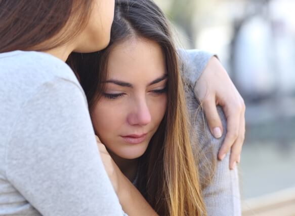 Young girl suffering from addiction to opiates being held by her friend