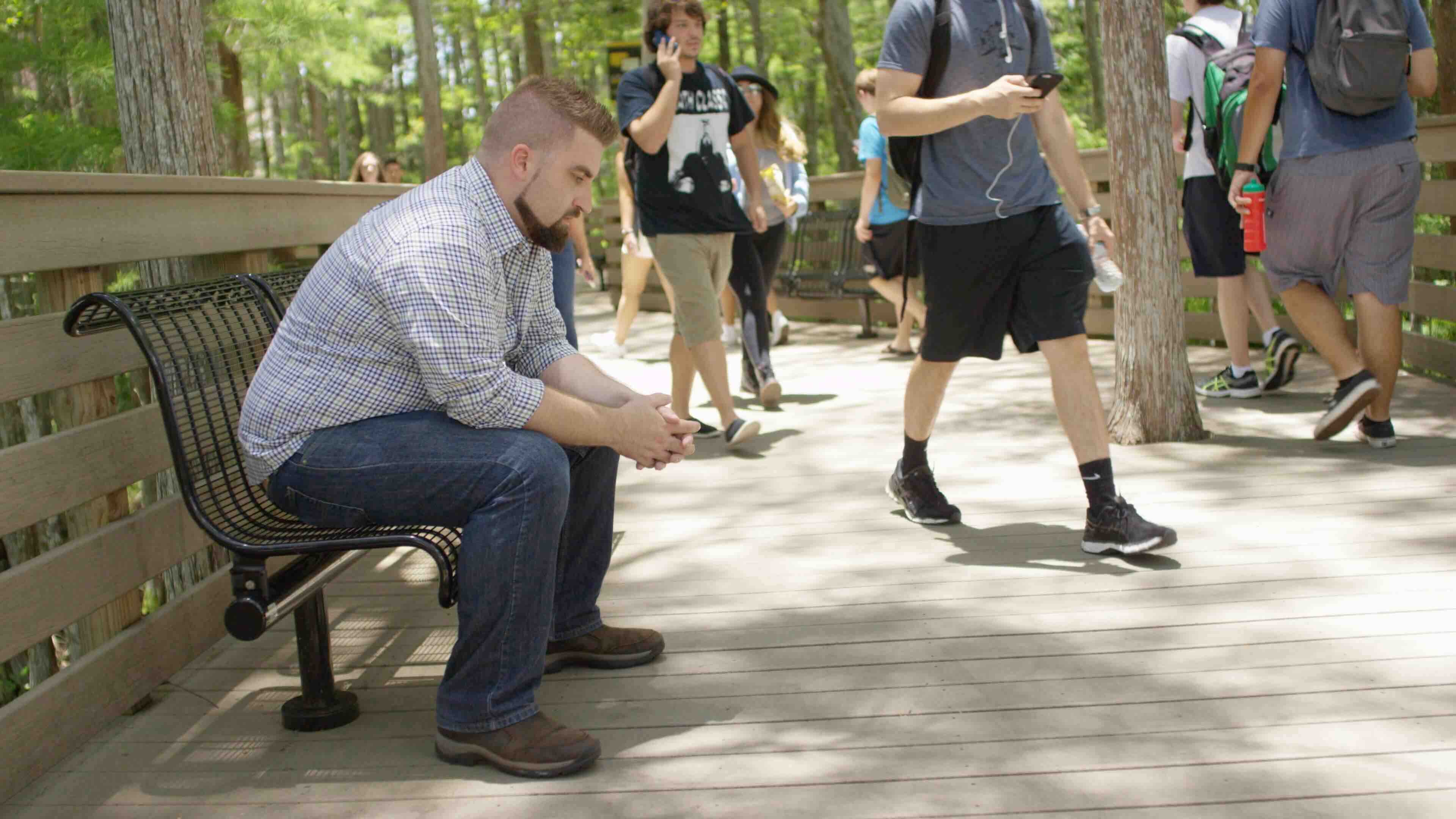 Stressed man sitting on the bench as people walk by