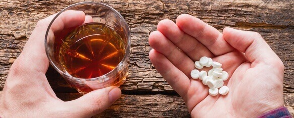 A person holding pills in one hand and alcohol in the other